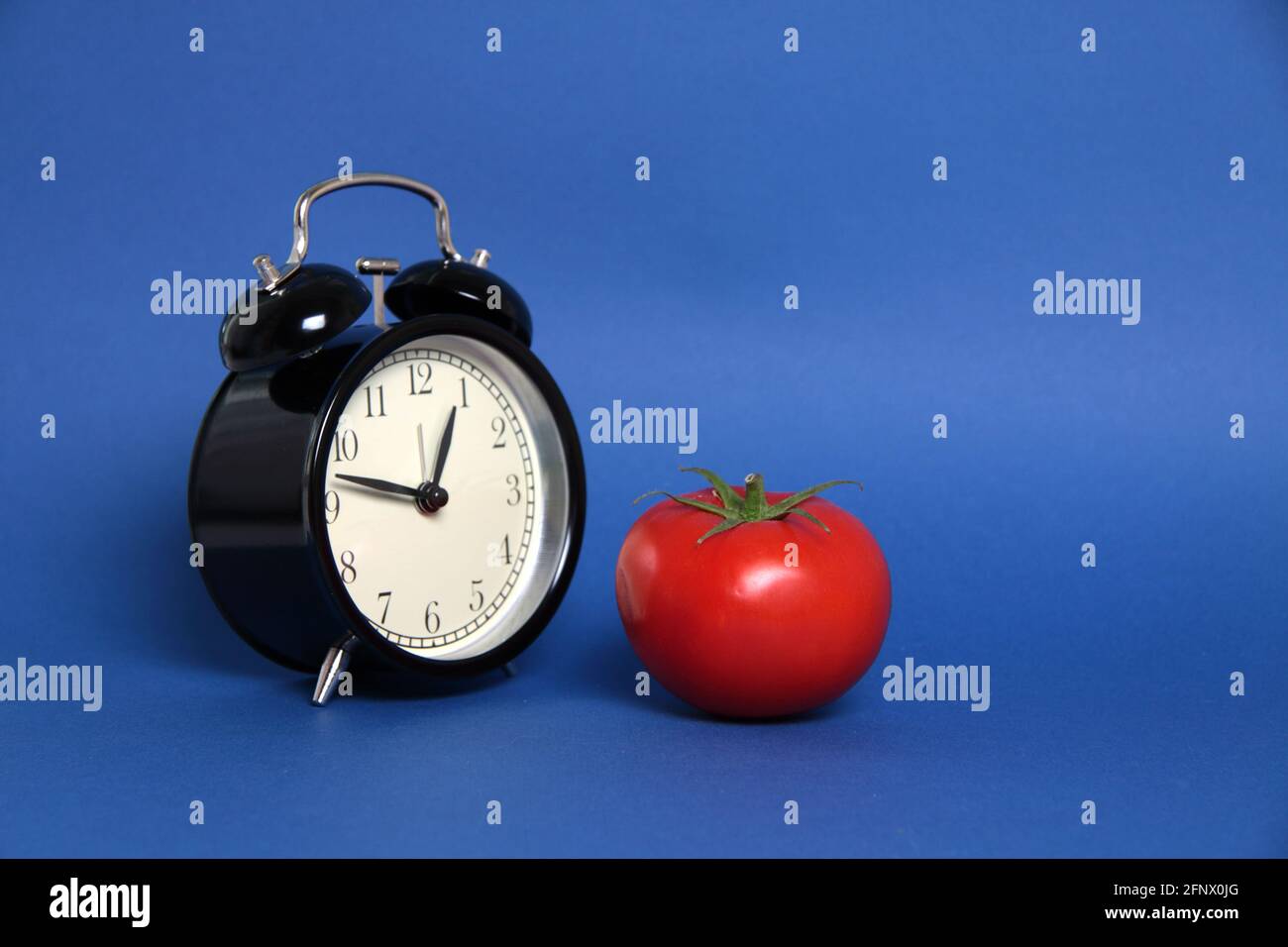 Pomodoro Technique concept - tomato and alarm clock isolated on blue background. Time management techniques Stock Photo