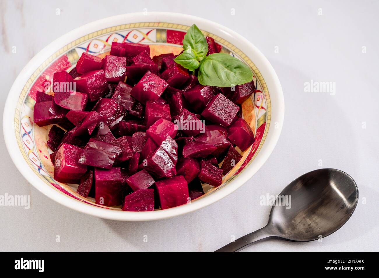 Beet salad with olive oil and basil in a plate on a white marble background. Fresh and healthy vegetables concept. Stock Photo
