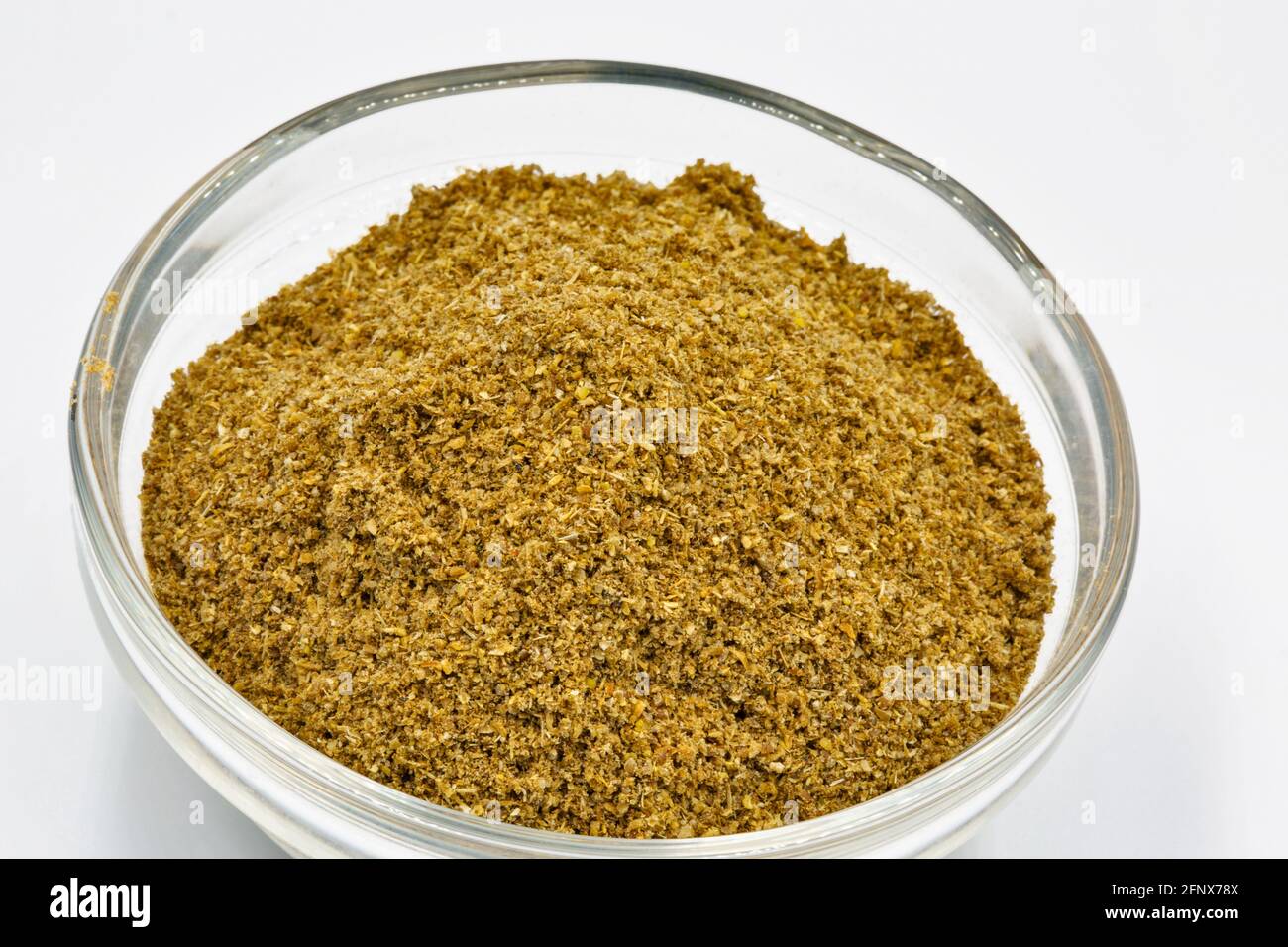 Ground cumin or coriander in glass bowl closeup against white