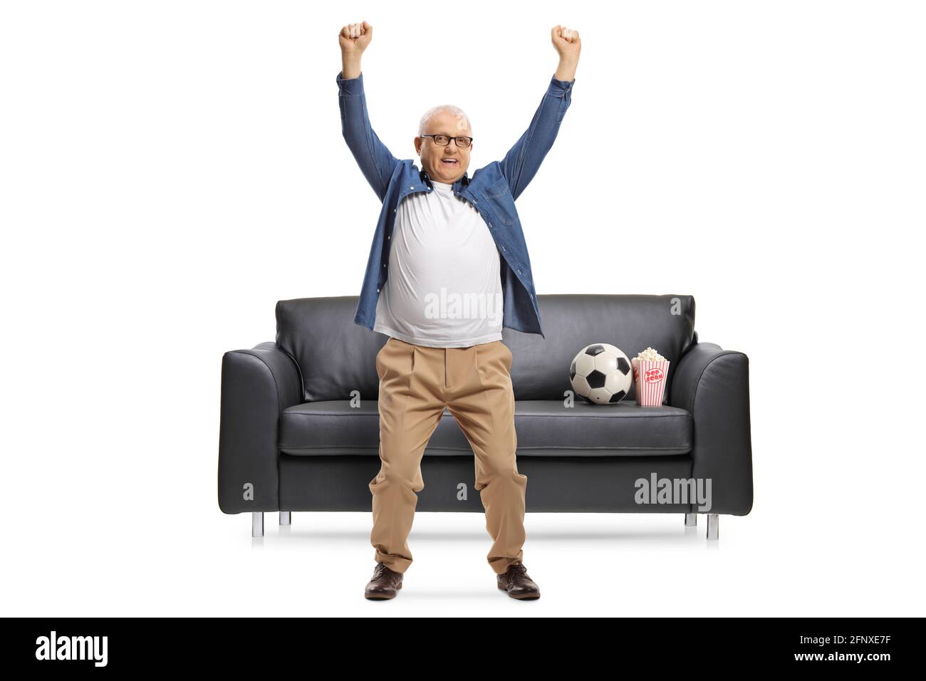 Mature football fan cheering in front of a black leather sofa isolated ...