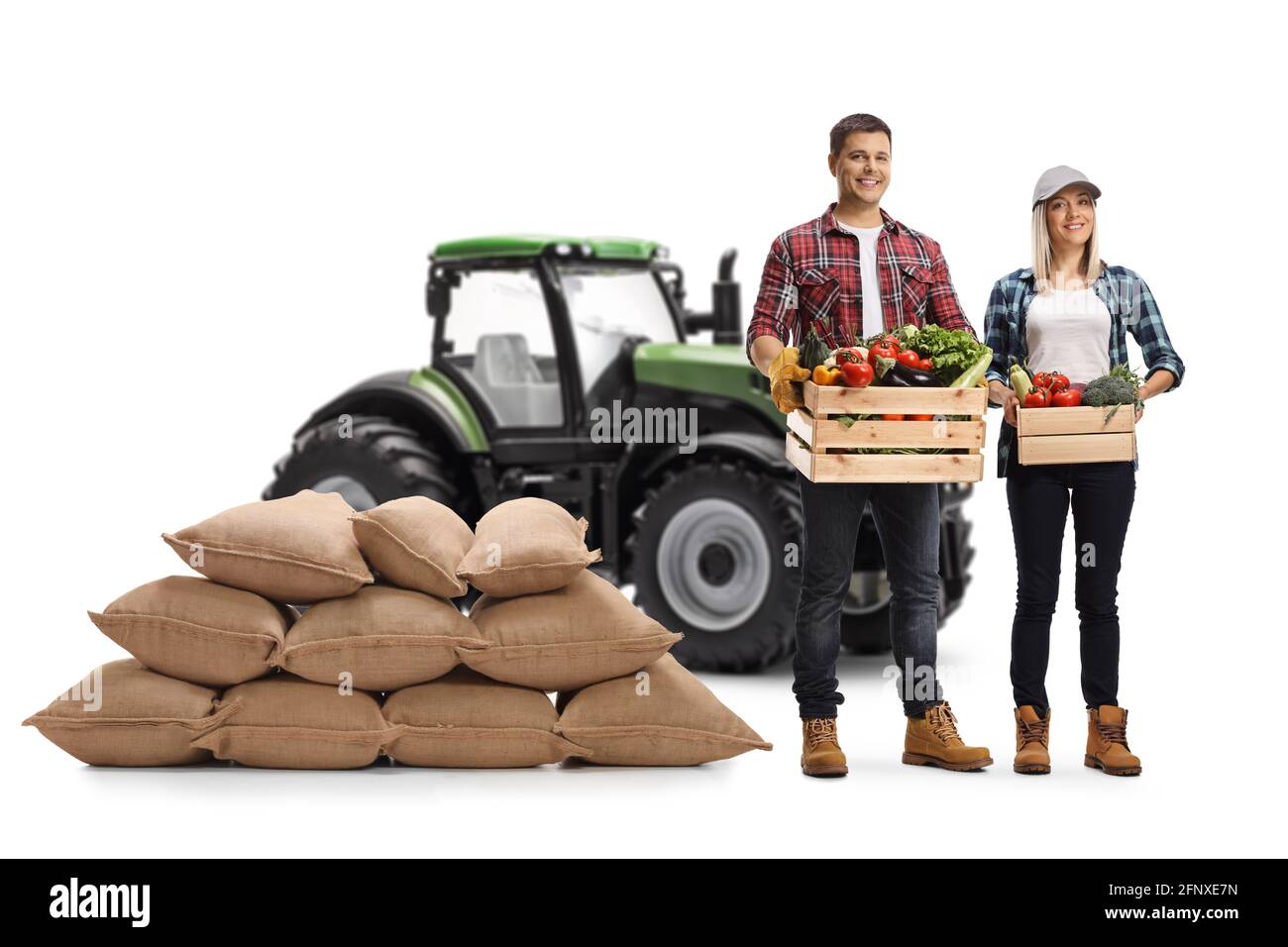 Young farmers carrying crates with vegetables and posing in front of a tractor isolated on white background Stock Photo