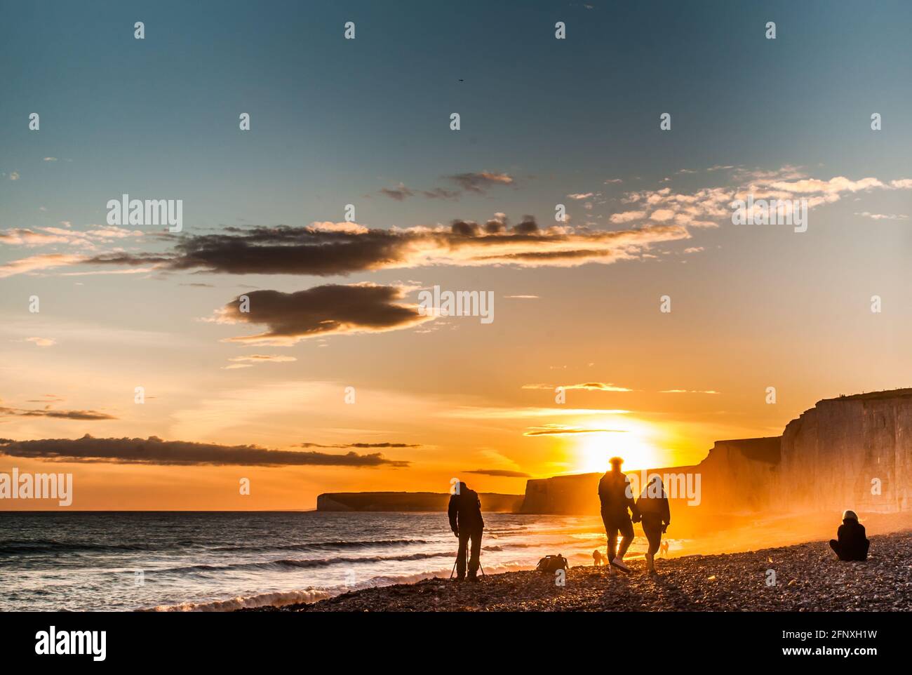 Birling Gap, Eastbourne, East Sussex, UK. 19th May, 2021. Glorious sunset over the Seven Sisters chalk cliffs beneath scattered clouds. Couple walk hand in hand on the beach past photographer capturing the scene. Credit: David Burr/Alamy Live News Stock Photo
