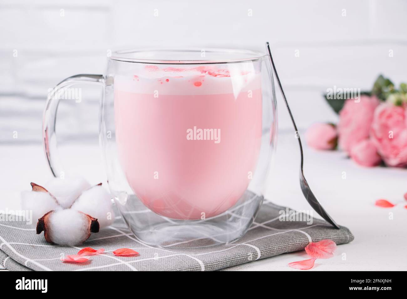 Pink matcha with rose petals on a white background. Transparent cup