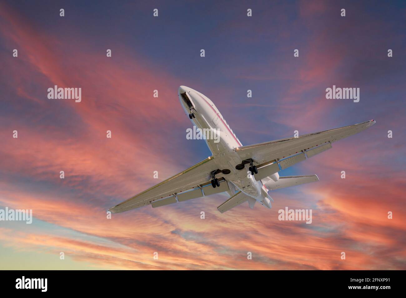 Airplane in the sky at sunrise or sunset. Small business jet is flying with lights and deployed landing gear preparing for landing or after takeoff Stock Photo