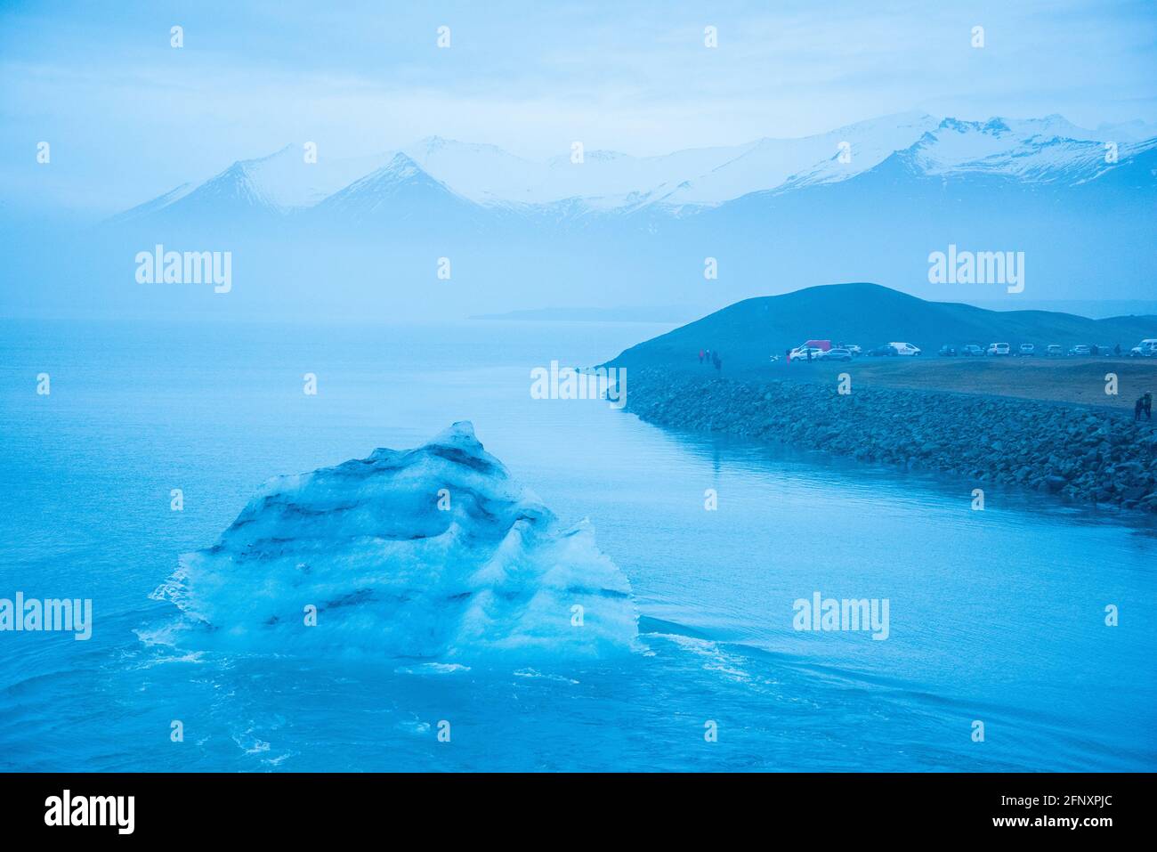 Icelandic glacier floating from global warming effects. Foggy atmosphere with snowcapped mountain range in the distance. Iceberg has layers of volcani Stock Photo