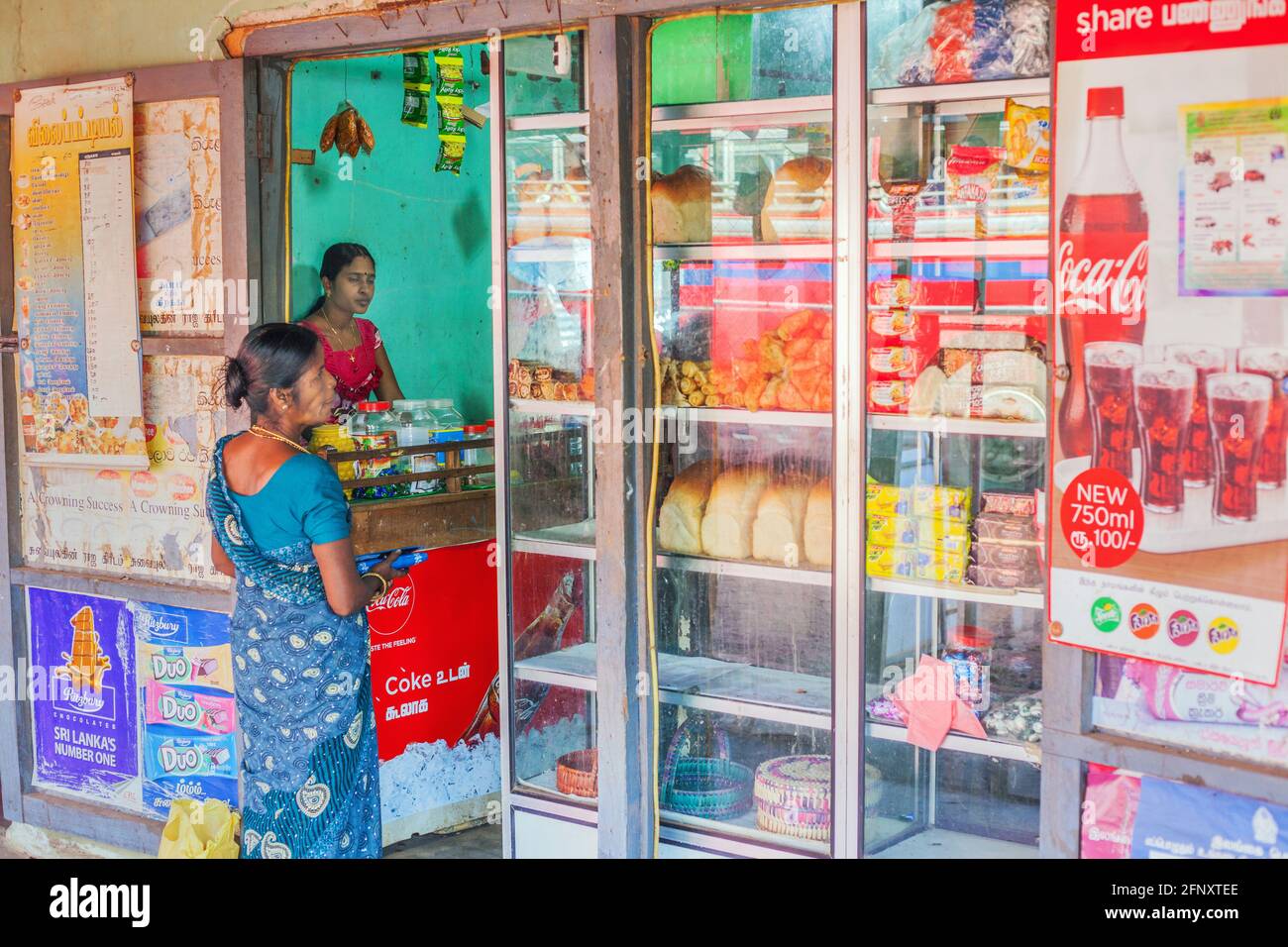 Sri Lankan female standing at shop doorway looking at items displayed in the window, Mullaitivu, Northern Province, Sri Lanka Stock Photo
