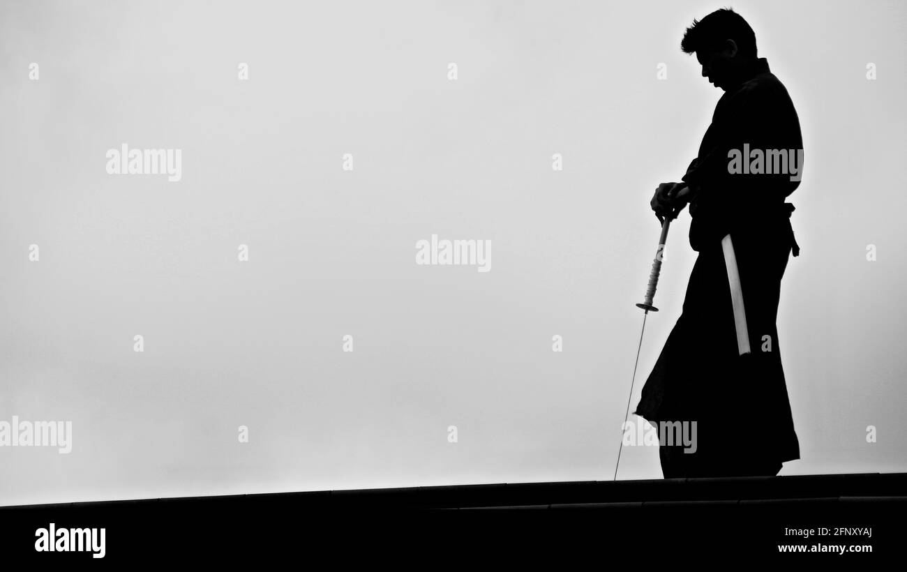 Silhouette of a samurai in an urban setting with a katana in a white scabbard. Stock Photo