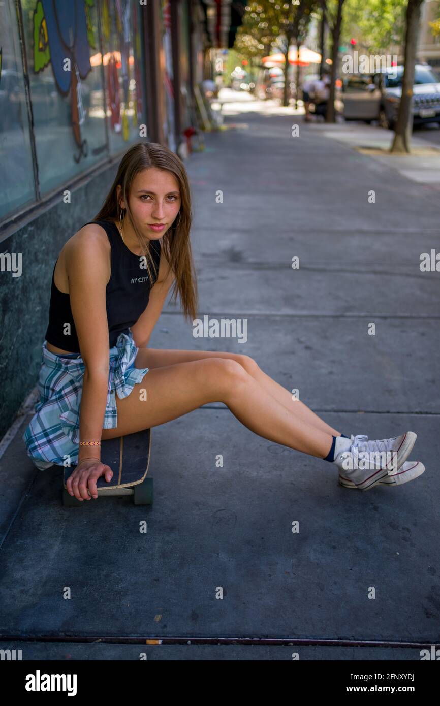 Young Woman Seated with Skateboard in Downtown Urban Setting Stock Photo