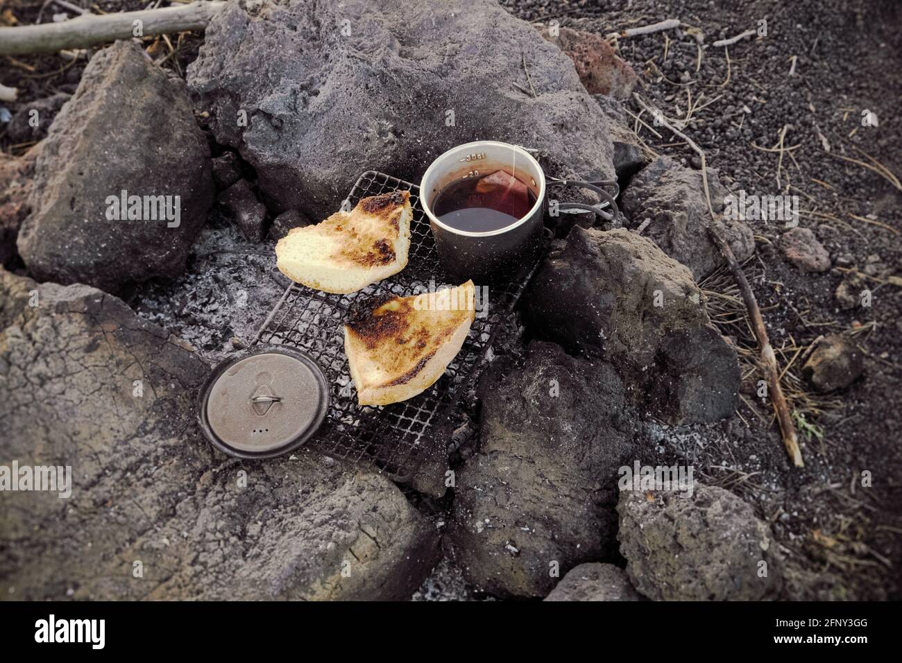 camp fire, food and cooking in recreational outdoor activity small grill with bread and mug of tea for the breakfast Stock Photo
