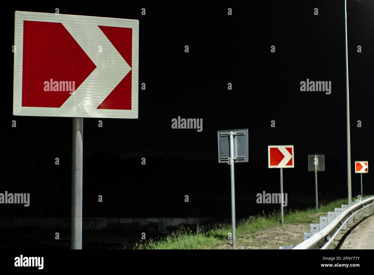 Right turn signs on the night road. Road signs warn of sharp turns in the light of streetlights Stock Photo