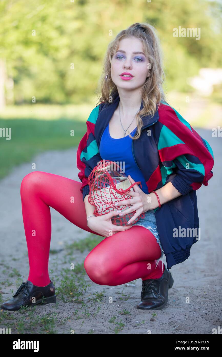 A beautiful 90s country girl in bright clothes holds a string bag with a  can of birch sap. Russian Woman in the style of the 90s Stock Photo - Alamy