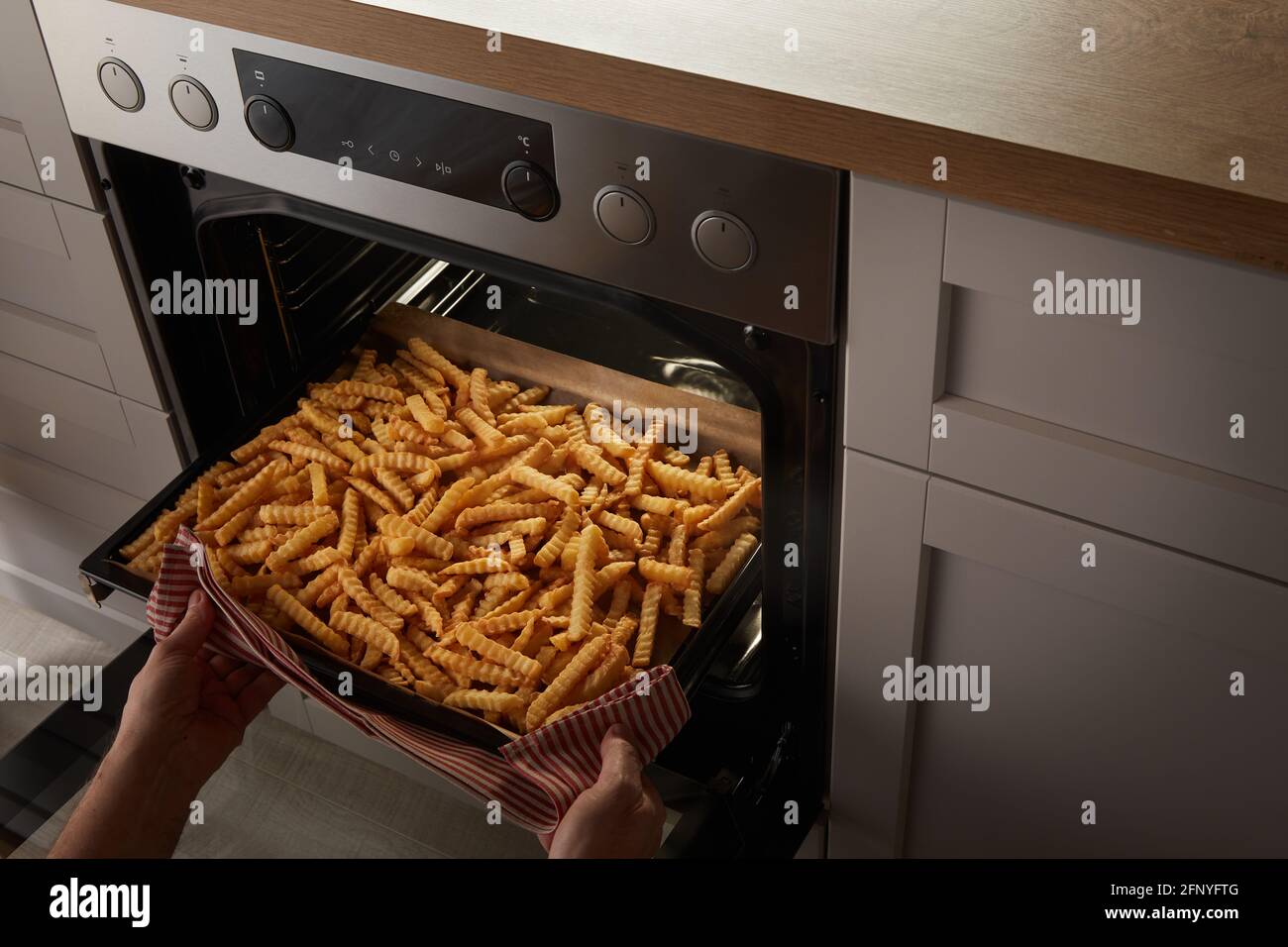 From above anonymous person with towel taking tray with crispy crinkle fries from hot stove Stock Photo