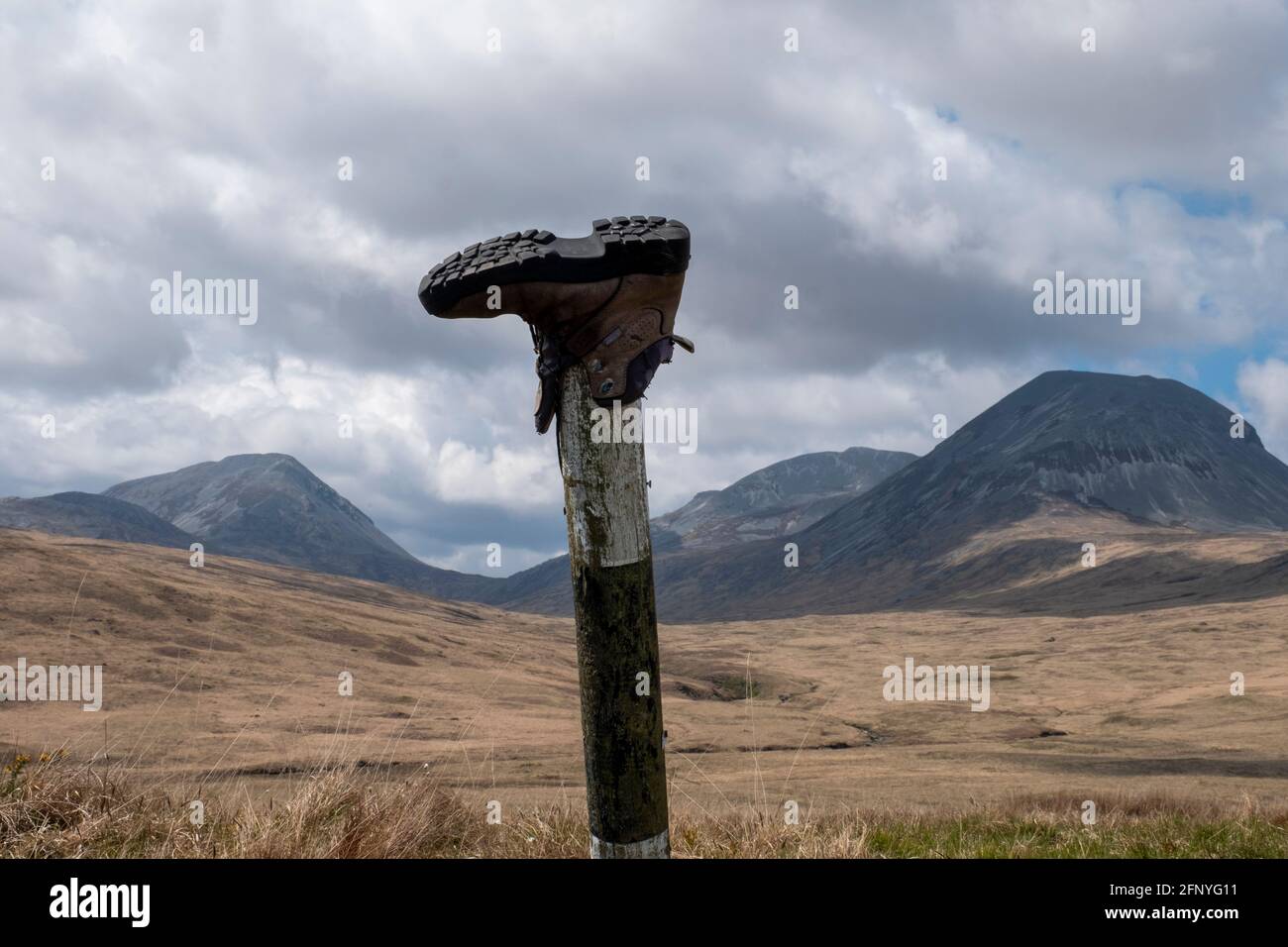 A discarded walking boot on a roadside marker pole with the Paps of Jura in the distance, Isle of Jura, Inner Hebrides, Scotland. Stock Photo