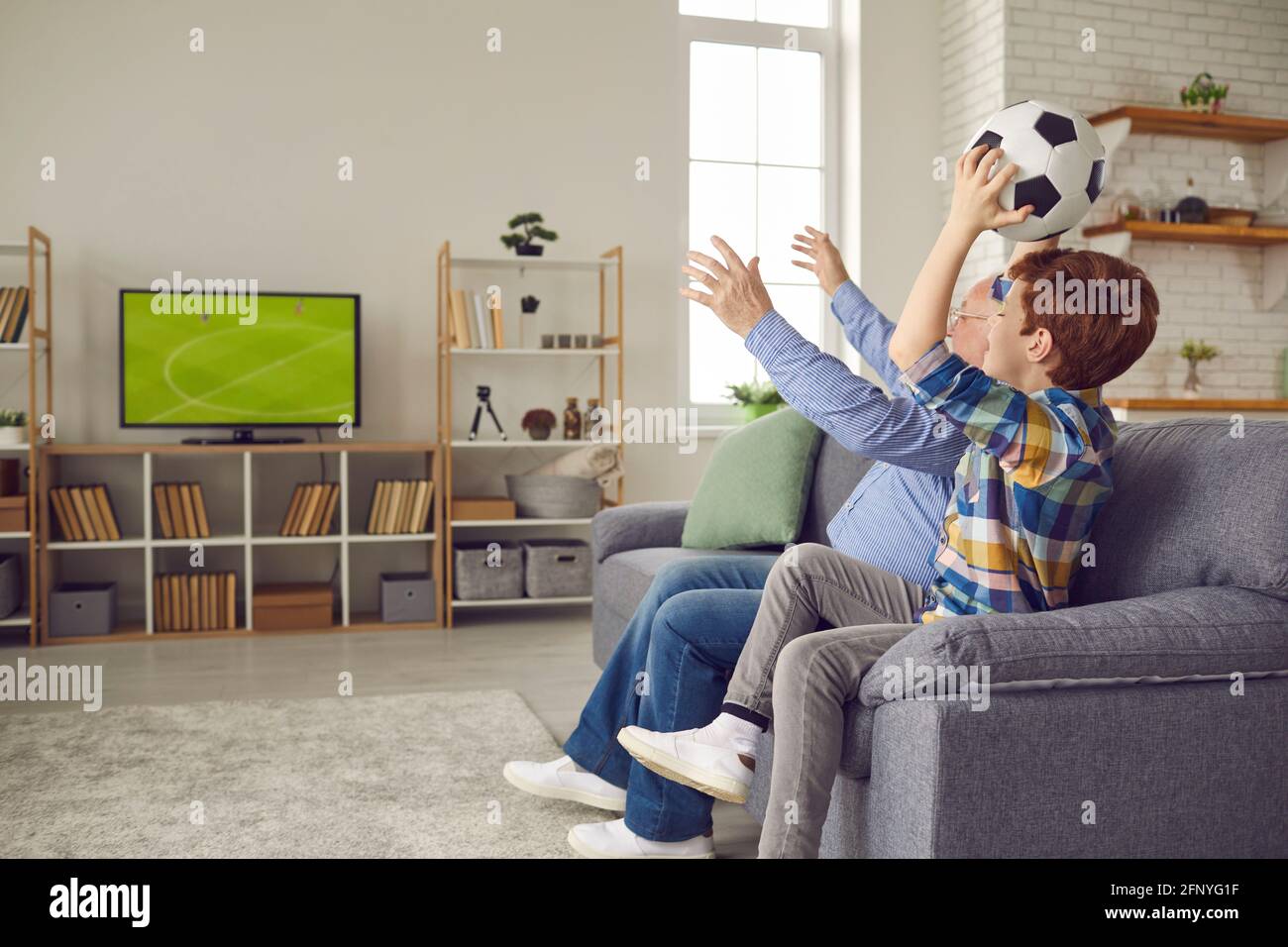 Senior grandfather and preteen grandson fan watching soccer match at home Stock Photo