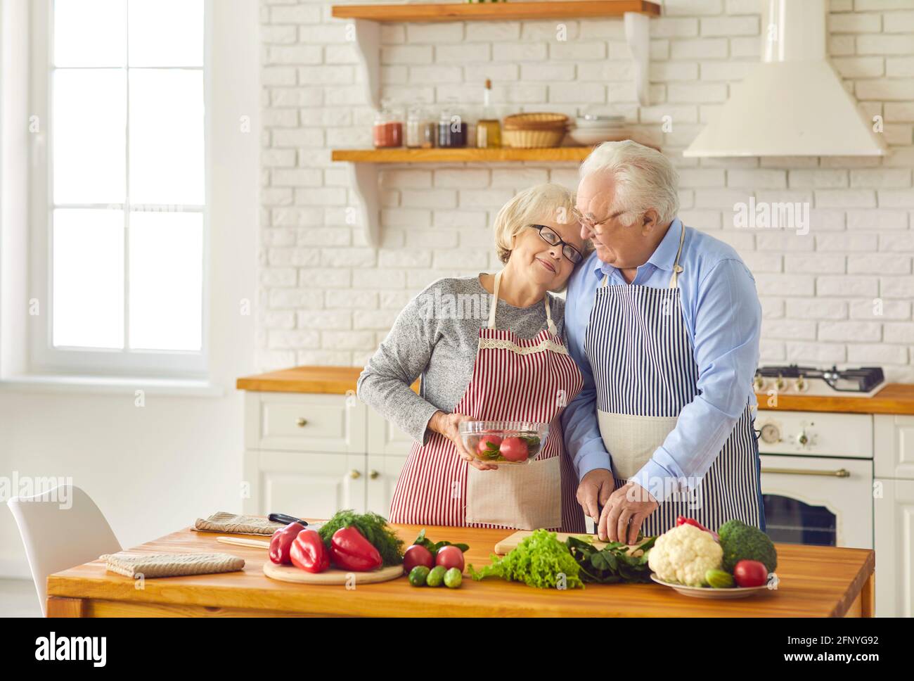 Mature loving couple in cooking aprons hugging and cooking healthy vegetarian diet dish Stock Photo