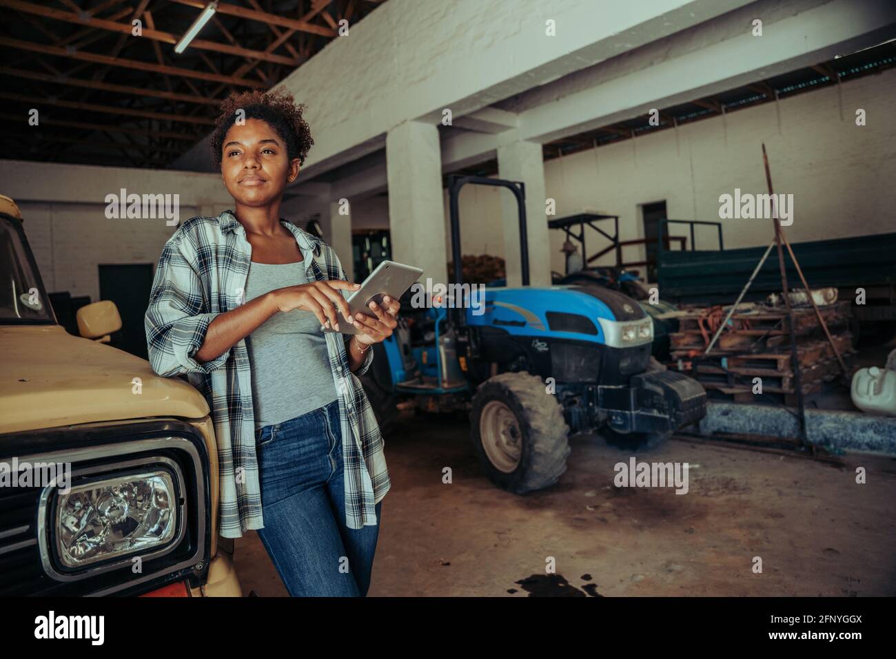 Mixed race female wearing checkered flannel carrying digital tablet in barn Stock Photo