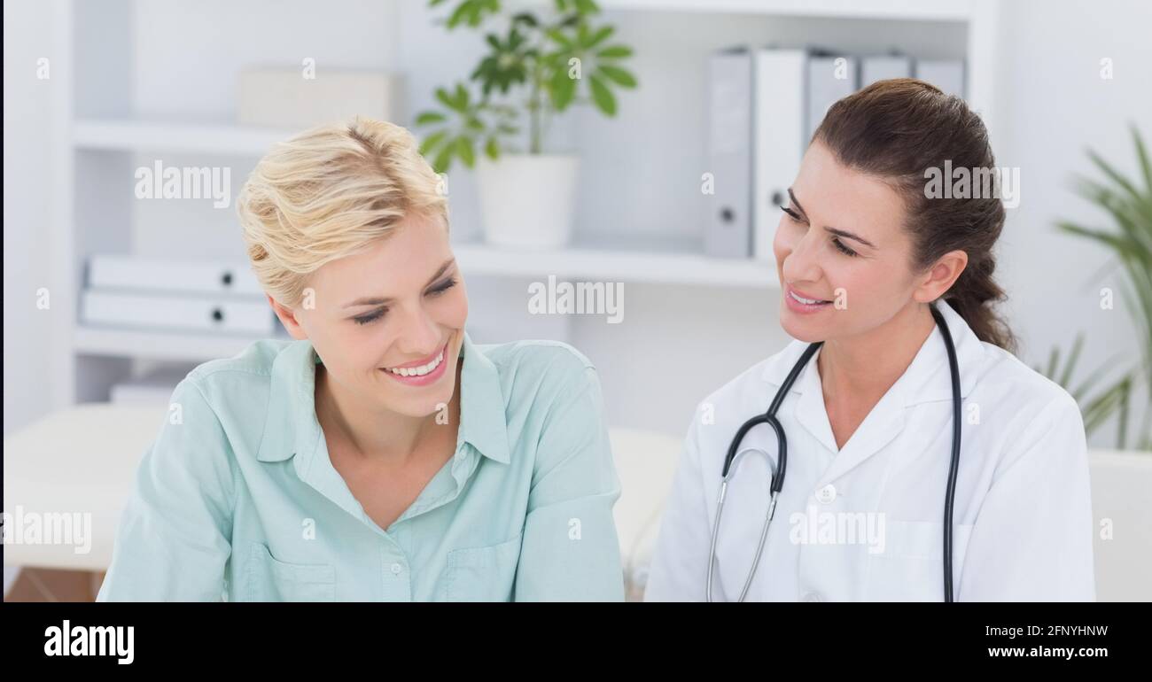 Caucasian female doctor and female patient smiling while sitting at hospital Stock Photo