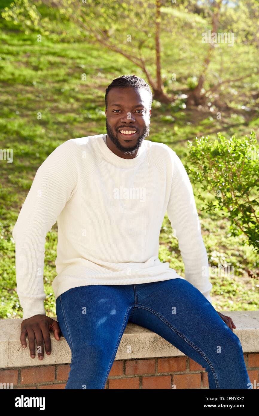 Young African American man smiling sitting on a wall. Happy Latino man. High quality photo Stock Photo