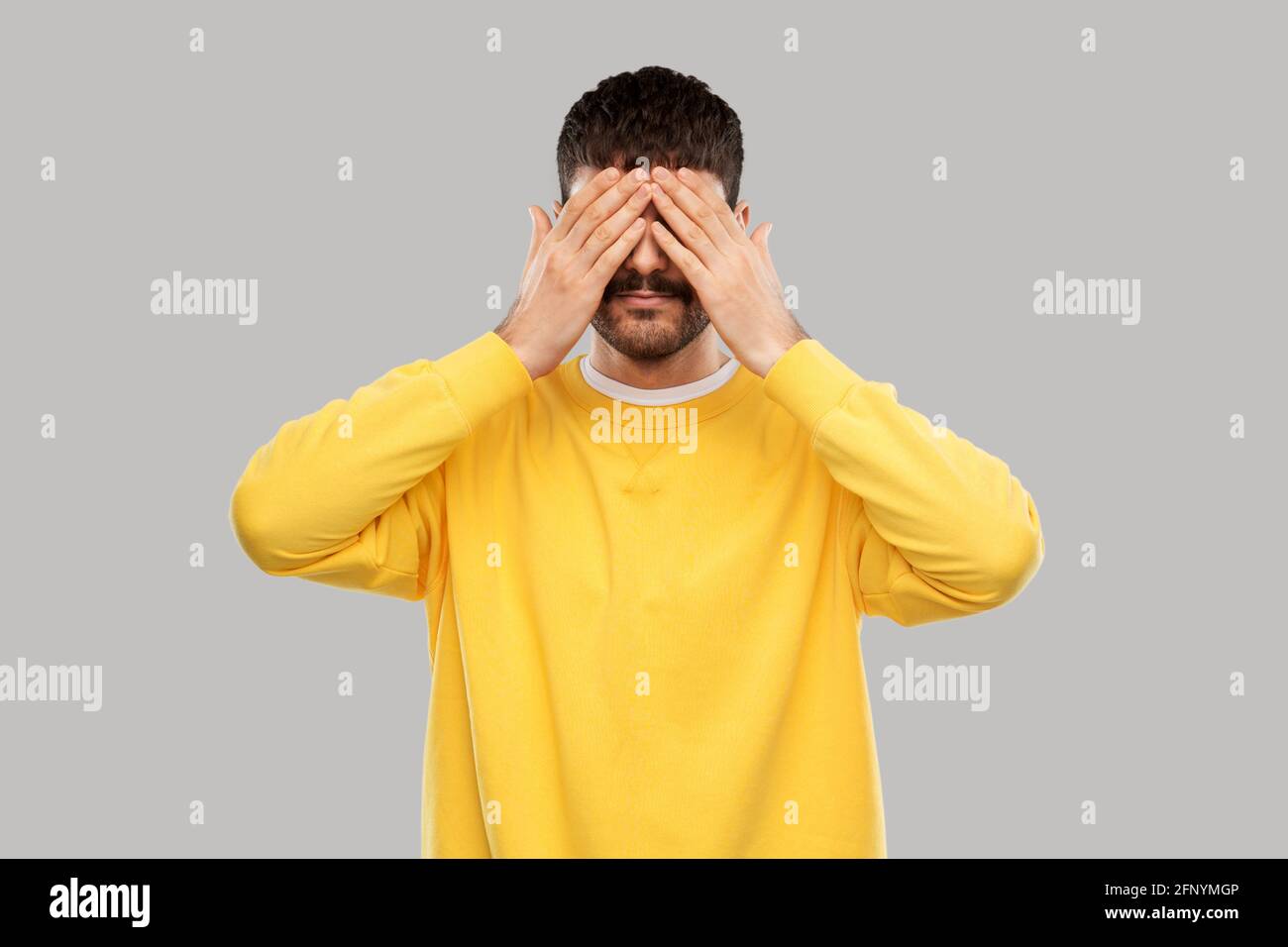 man in yellow sweatshirt closing his eyes by hands Stock Photo
