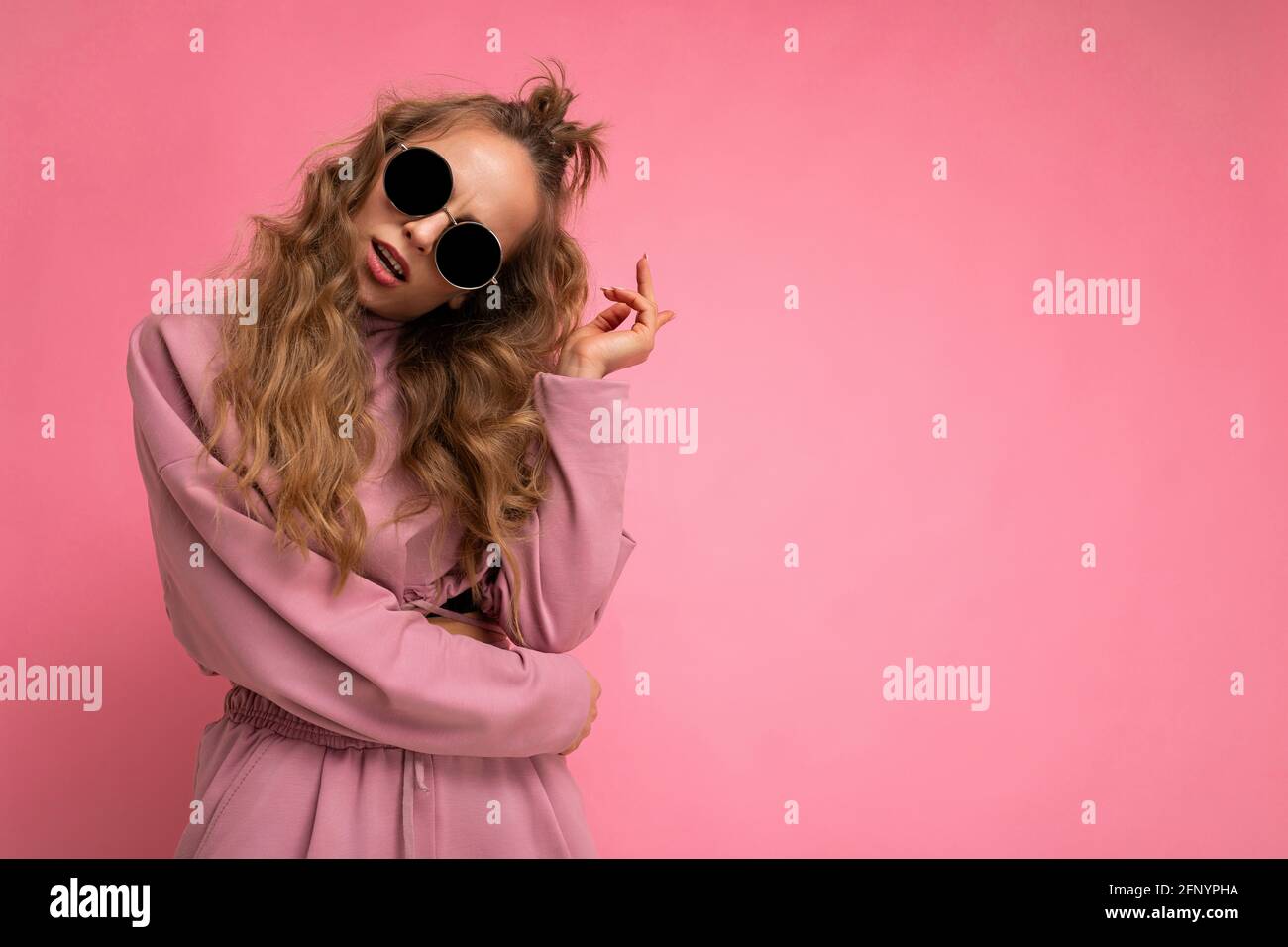 Photo shot of beautiful young dark blonde woman wearing casual clothes and stylish sunglasses isolated over colorful background looking at camera Stock Photo
