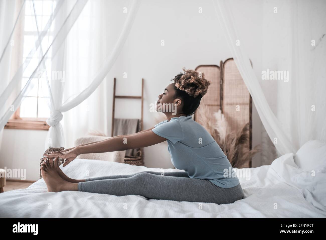 African american woman sitting on bed holding toes Stock Photo