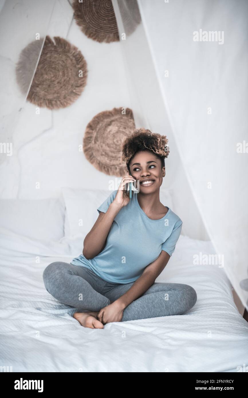 Happy woman talking on smartphone sitting on bed Stock Photo