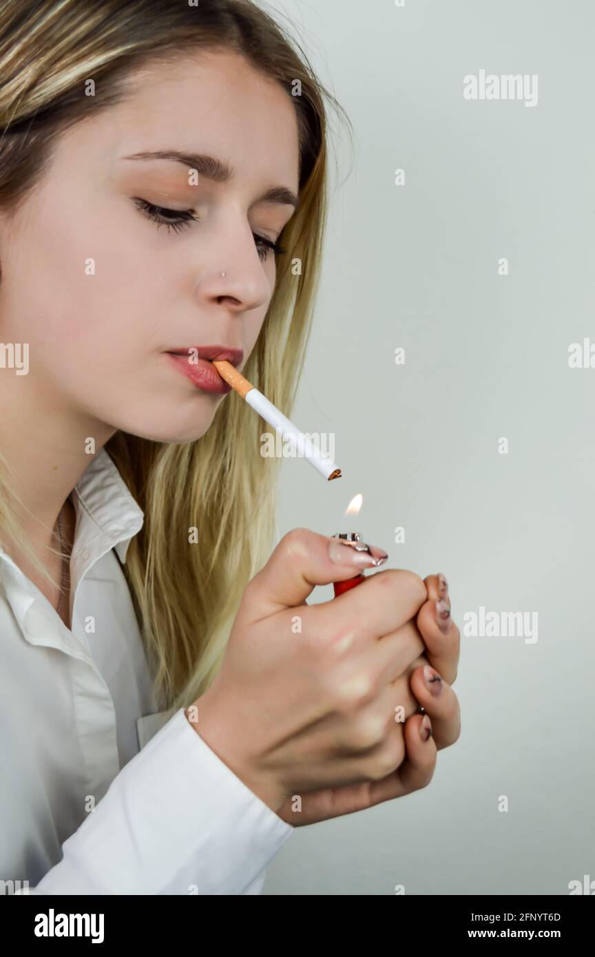 Portrait of a beautiful young blonde woman who lights a cigarette with