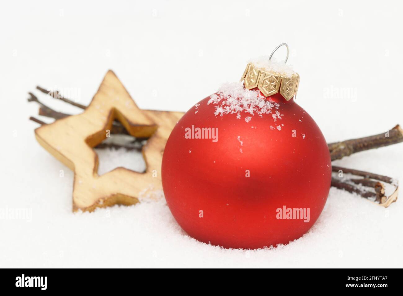red christmas ornament, branch and wooden star lying in snow Stock Photo