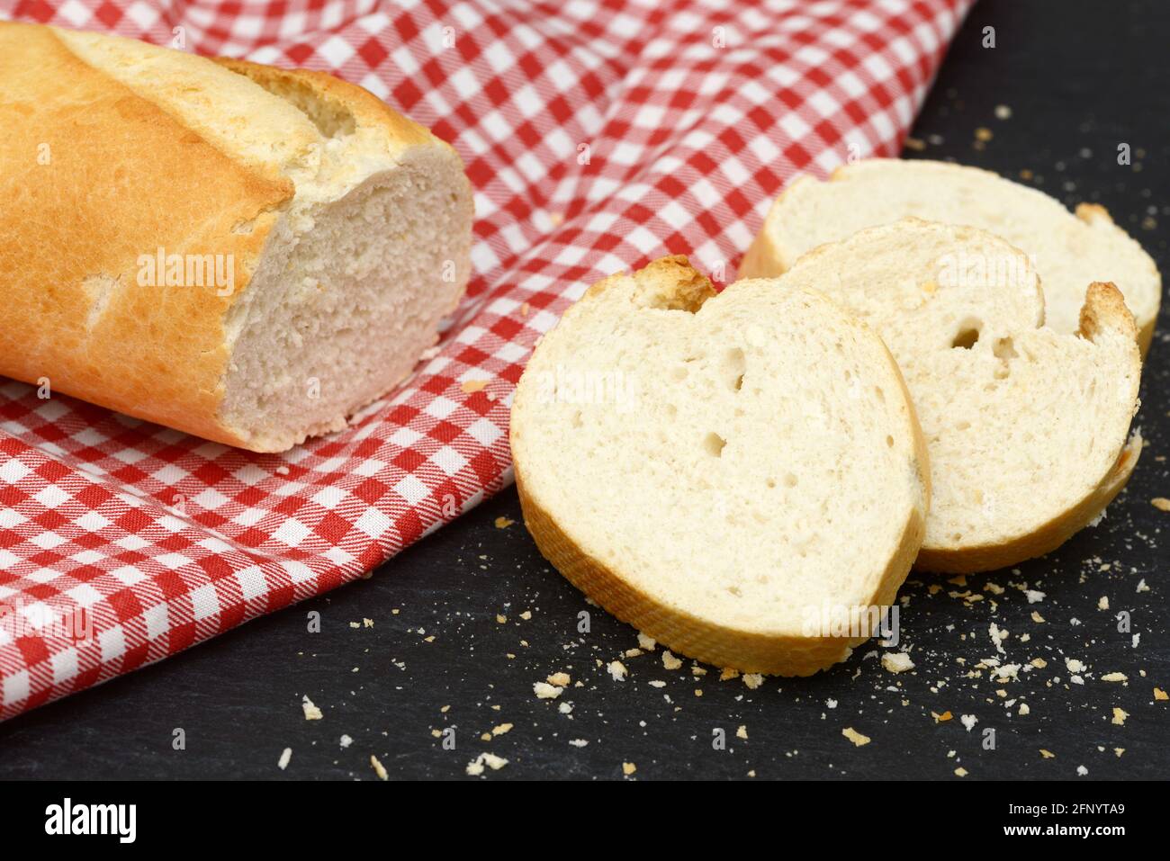 rustic crusty white bread lying on black slate on red white towel in the kitchen Stock Photo