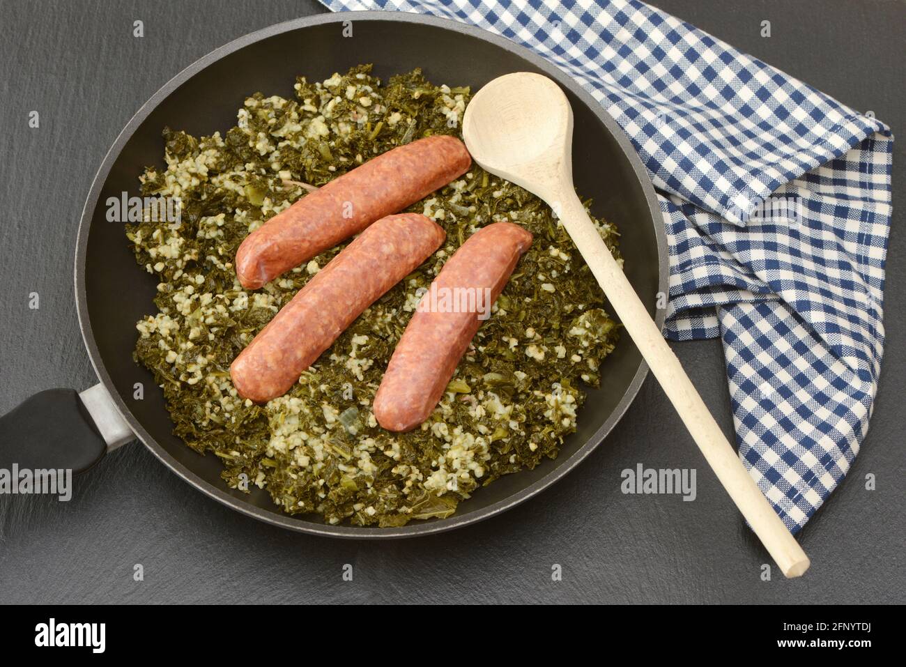 Fresh cooked kale with sausages and wooden spoon  in the pan on black background Stock Photo