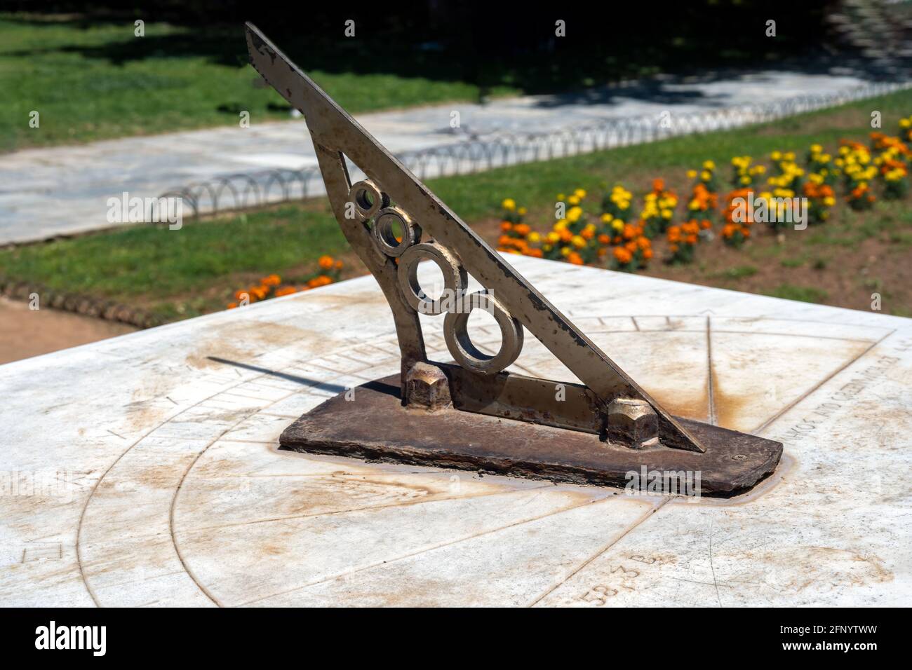 Old sundial at the National Garden public park, at the center of Athens-Greece. Antique astronomical sun clock with rusty steel gnomon dial on marble Stock Photo