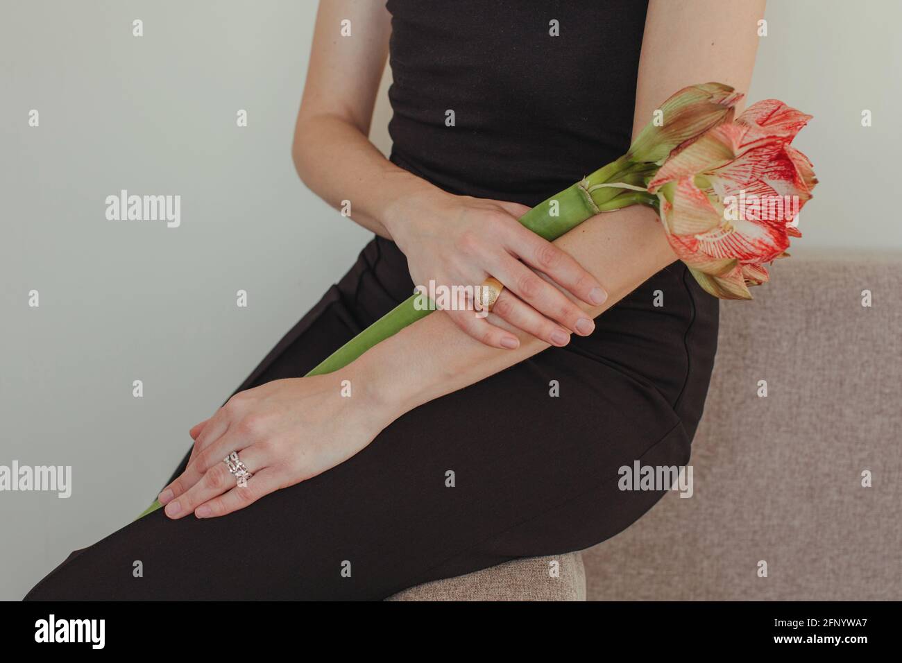 Close-up of a woman in an evening gown sitting on a sofa holding an Amaryllis flower Stock Photo