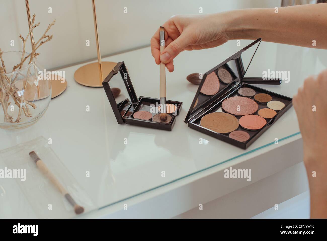 Close-up of a woman's hand dipping a make-up brush in a make-up palette on a dressing table Stock Photo