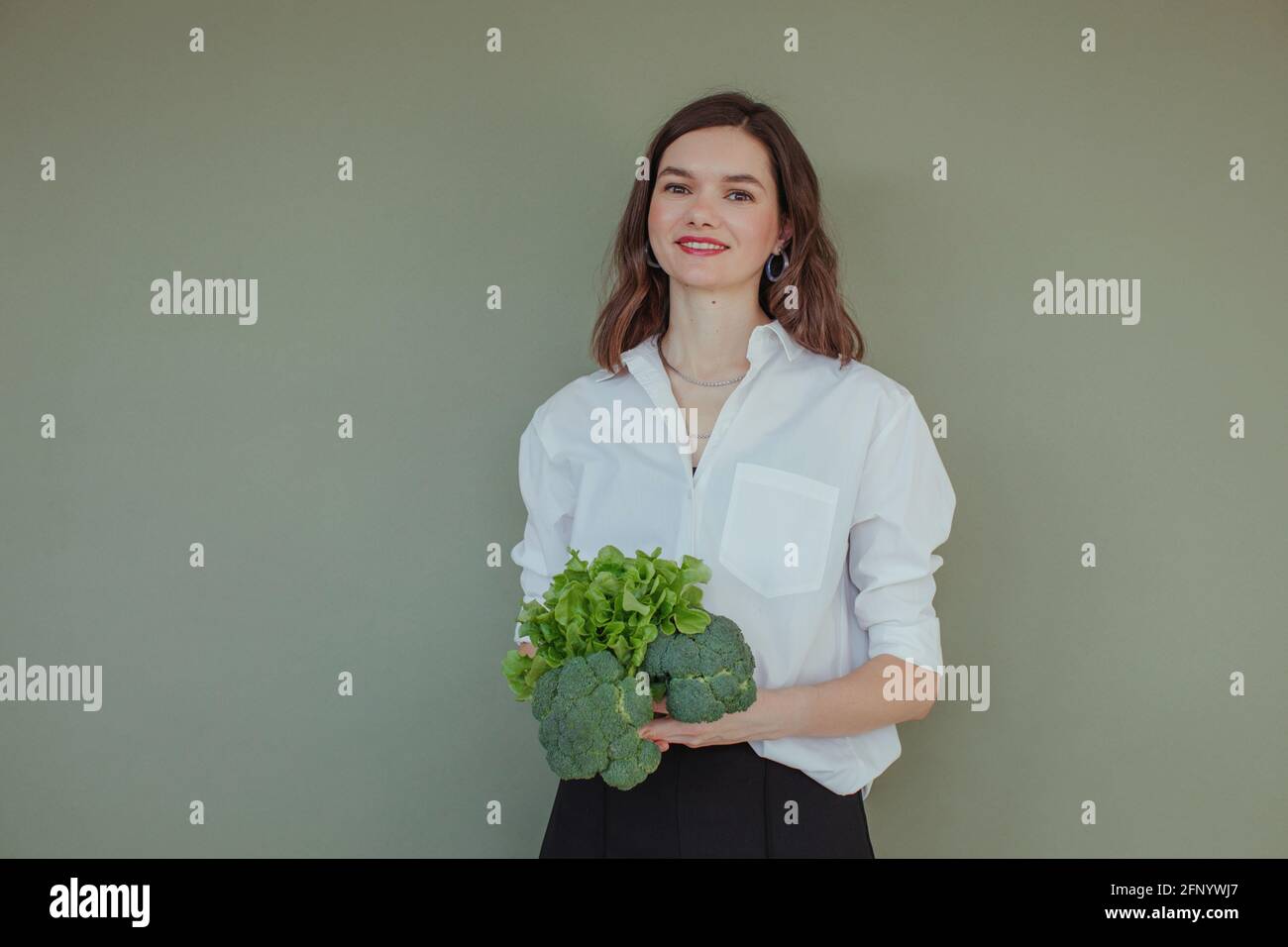 Portrait of a beautiful smiling woman holding fresh broccoli and lettuce Stock Photo