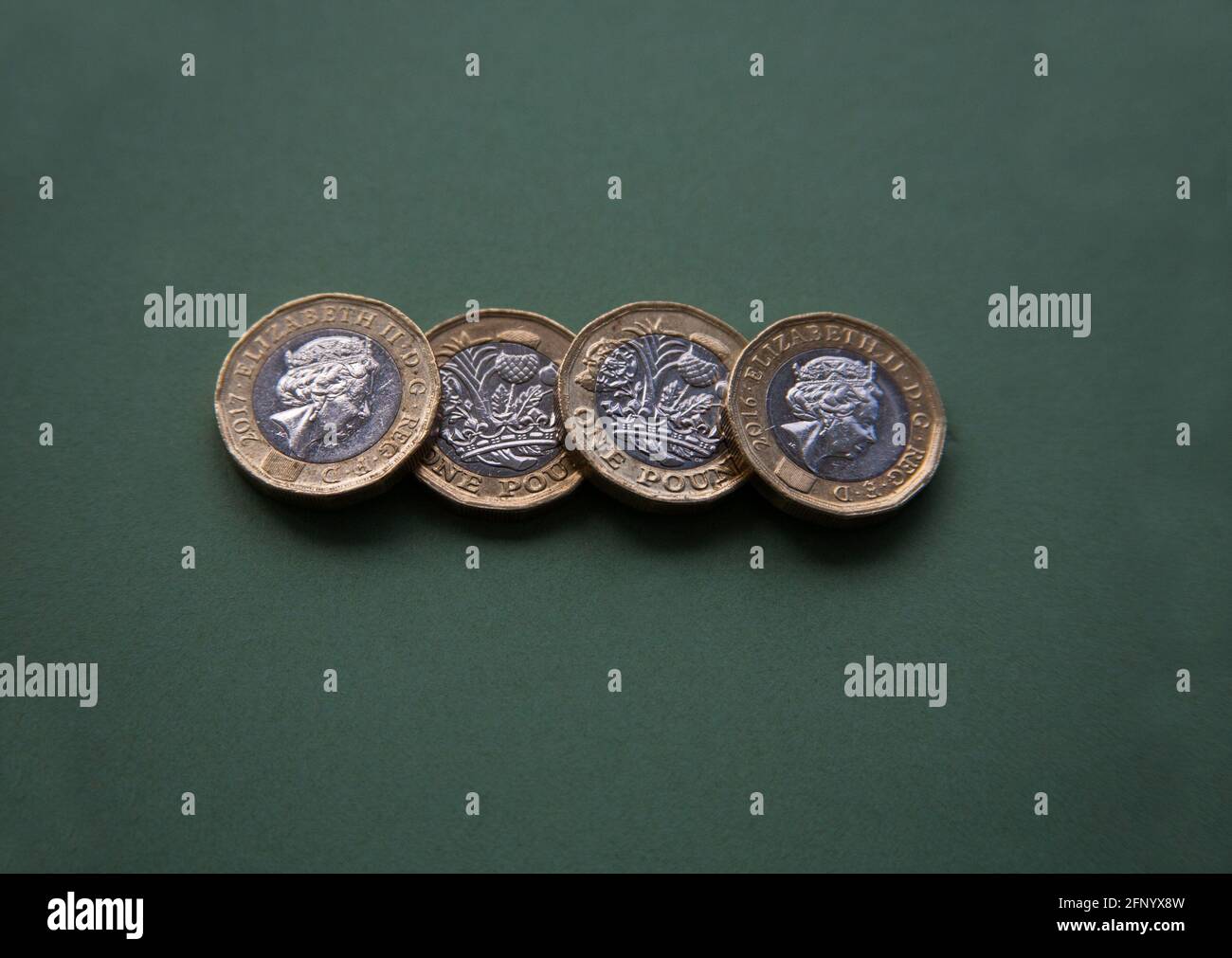 Four British sterling £1 coins in a row on green background Stock Photo