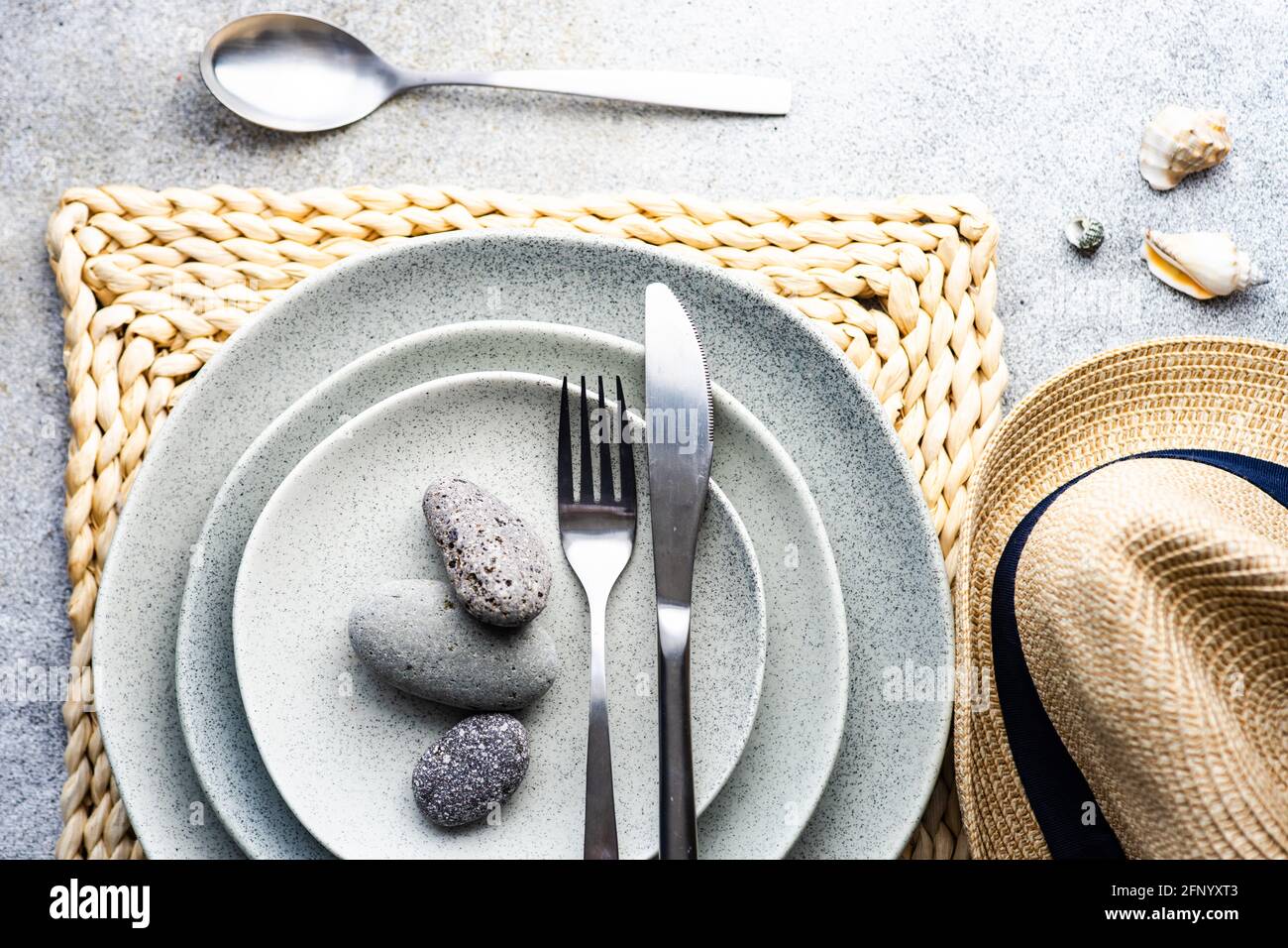 Overhead view of a rustic place setting with pebbles, seashells and a straw hat Stock Photo
