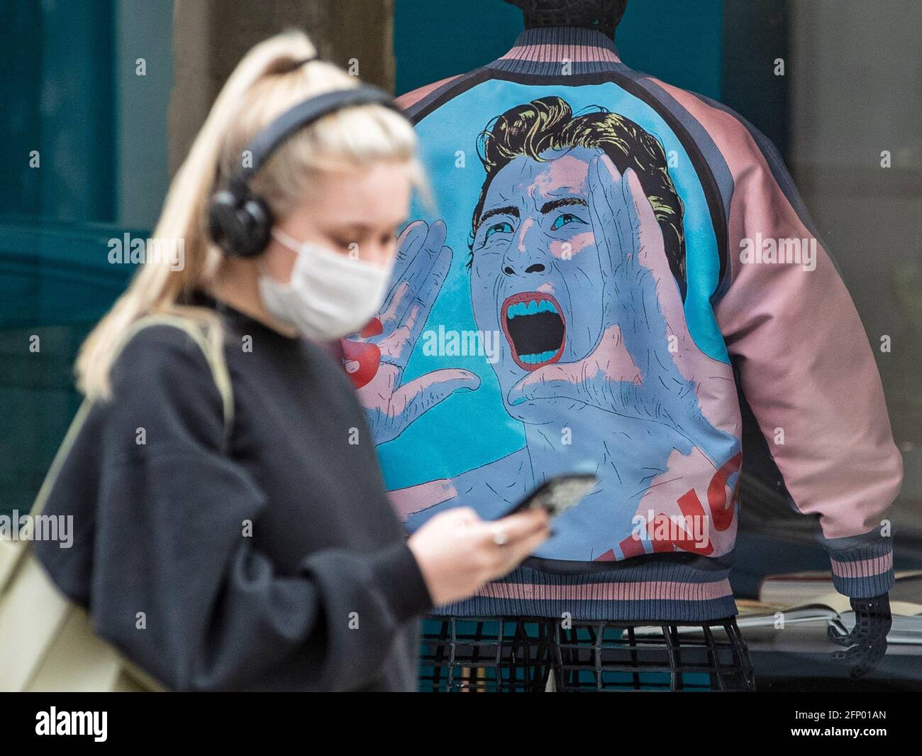 People walk past designer store Issey Miyake store in Central London with a jacket with face of man screaming in the background of the store. Stock Photo