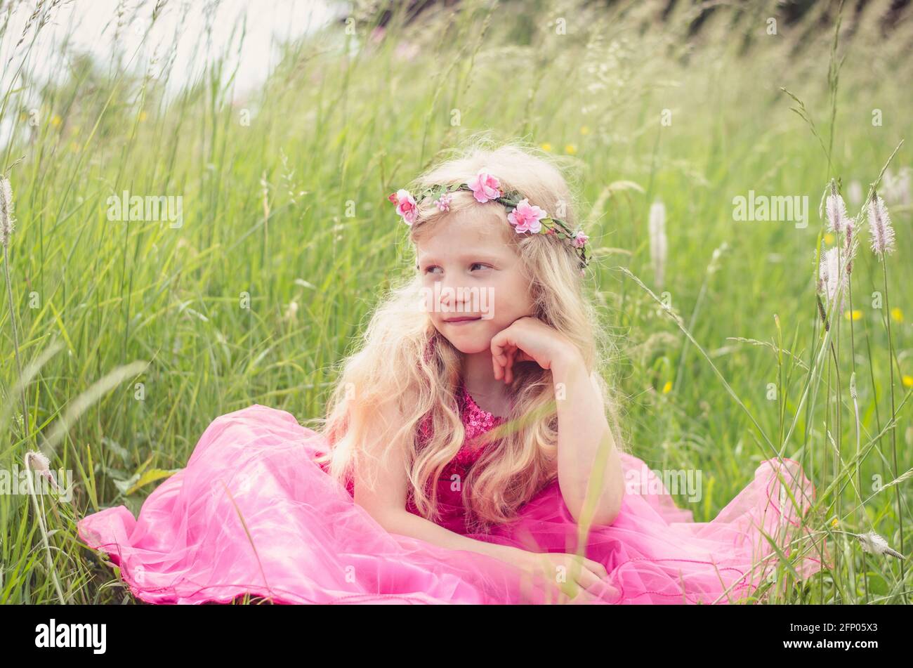 beautiful blond girl in pink dress thinking in the grass Stock Photo