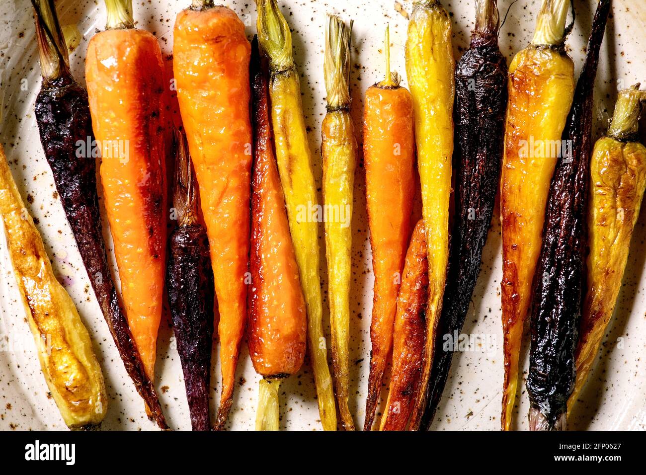 Grilled different colored carrots on ceramic plate. Top view, flat lay. Close up. Vegan dinner Stock Photo