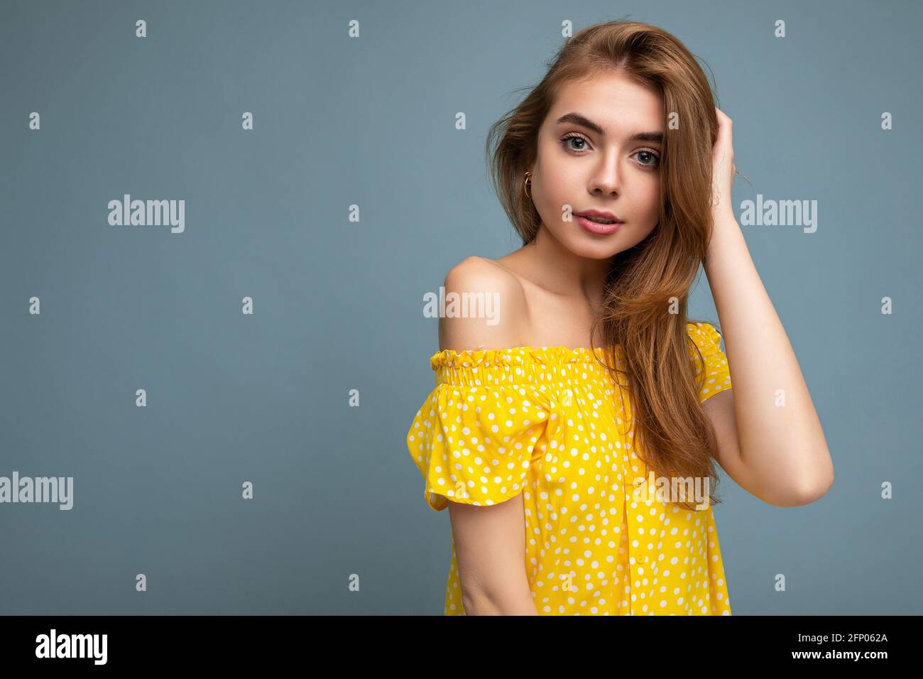 Young beautiful dark blonde woman with sincere emotions isolated on background wall with copy space wearing stylish summer yellow dress. Positive Stock Photo