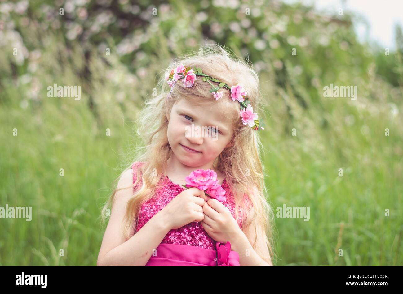 beautiful blond girl in pink dress holding two blossoming pink roses Stock Photo