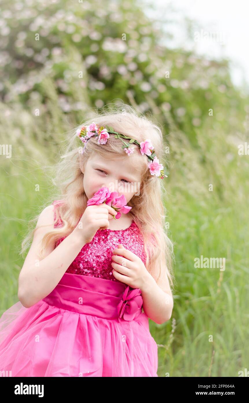 beautiful blond girl in pink dress holding pink rose flower Stock Photo
