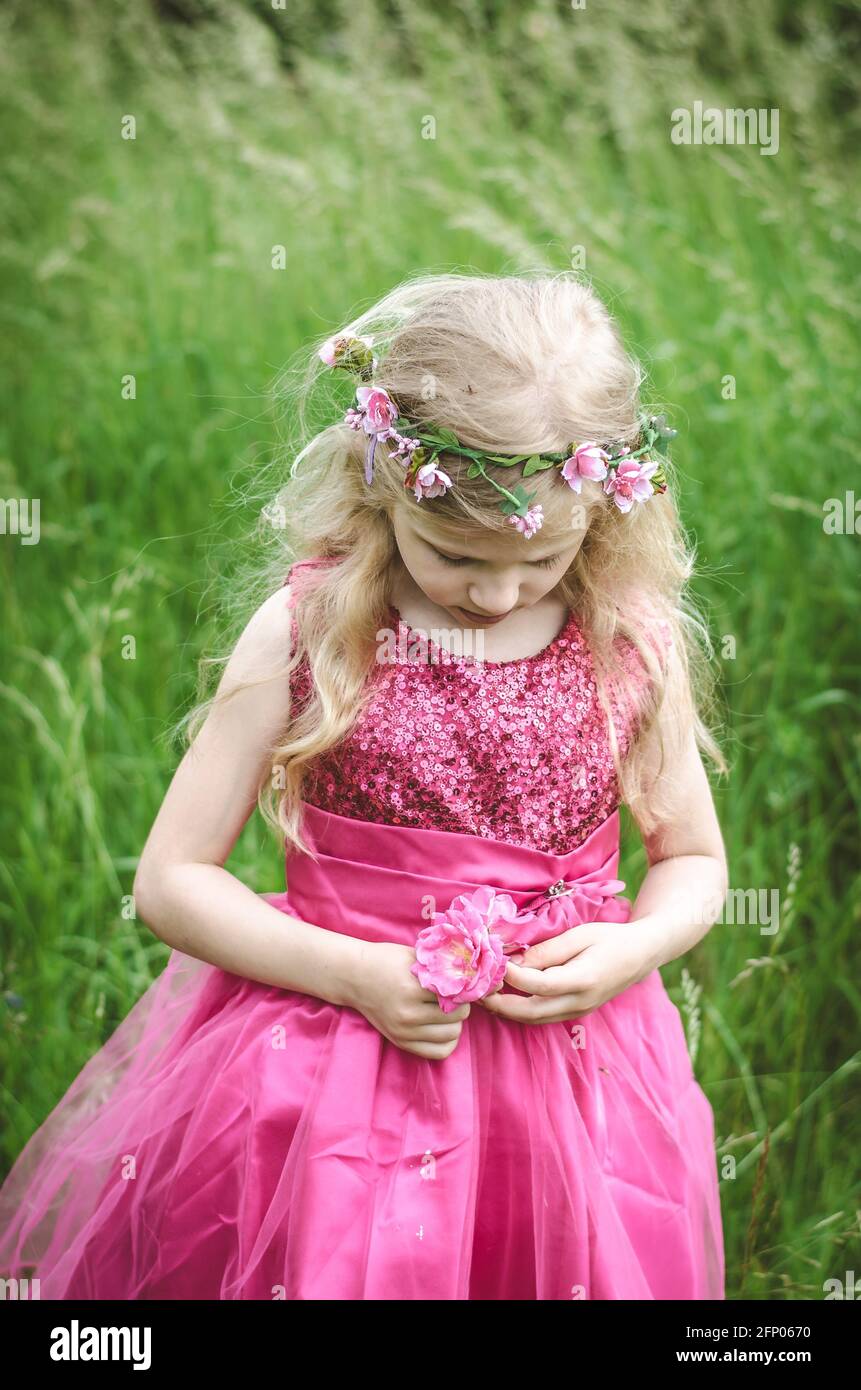 beautiful blond girl in pink dress with sad expression holding flower Stock Photo