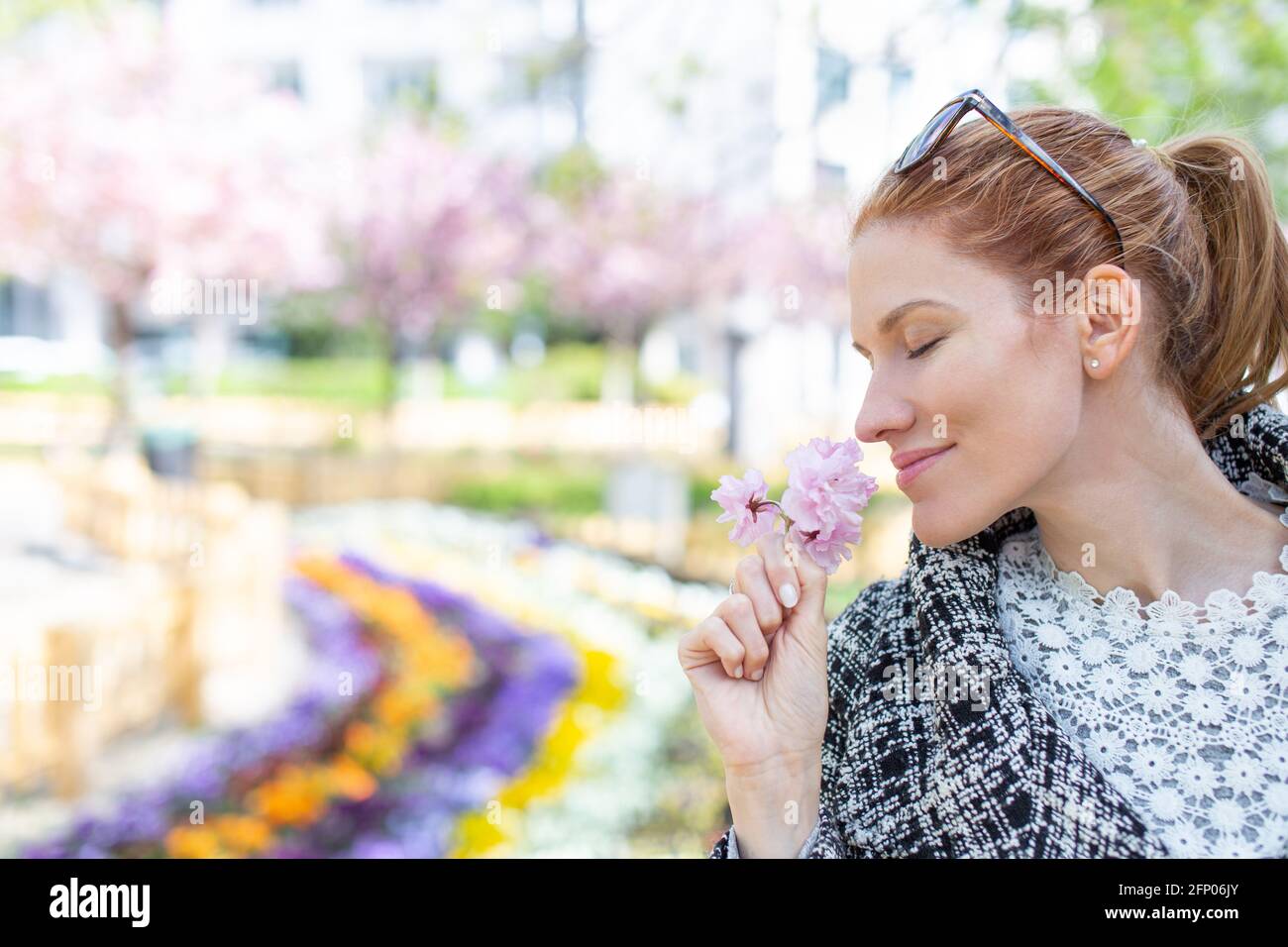 Cheerful young redhead woman smelling cherry blossom, empty space Stock Photo