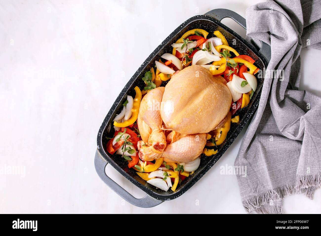 Raw organic uncooked whole chicken with sliced vegetables bell pepper, onion and herbs in oven tray with grey textile napkin, ready to cook. White mar Stock Photo