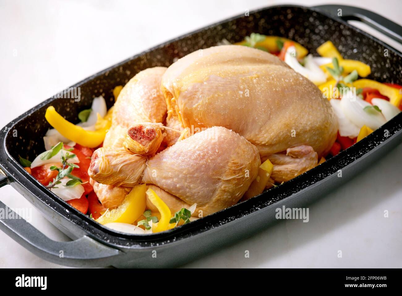Raw organic uncooked whole chicken with sliced vegetables bell pepper, onion and herbs in oven tray, ready to cook. White marble table. Stock Photo