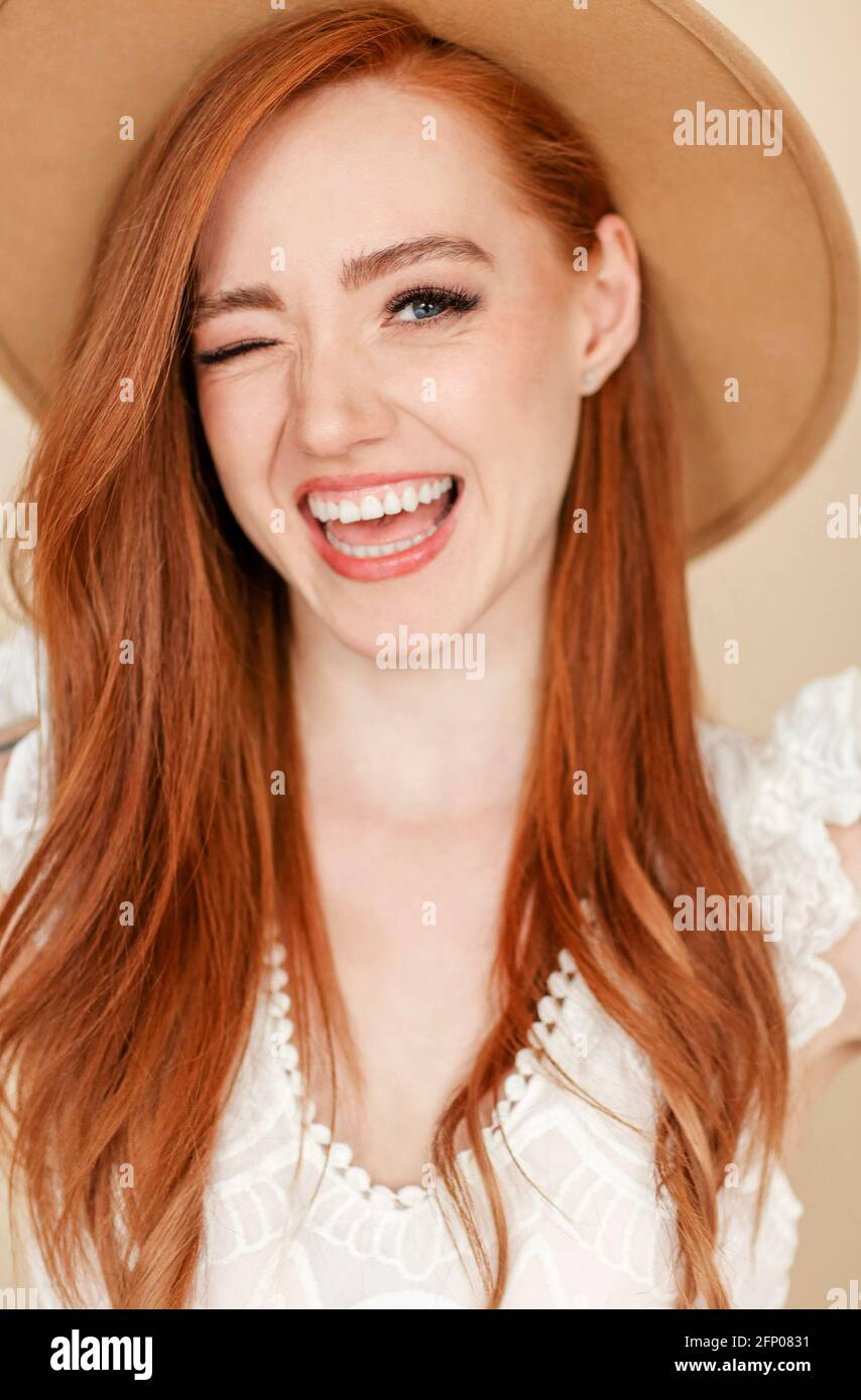 Happy redhead female with long hair and in stylish hat smiling and