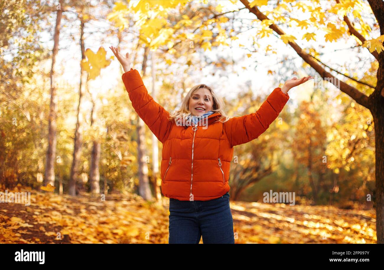 Delighted middle age female in outerwear smiling  on sunny weekend day in autumn park Stock Photo