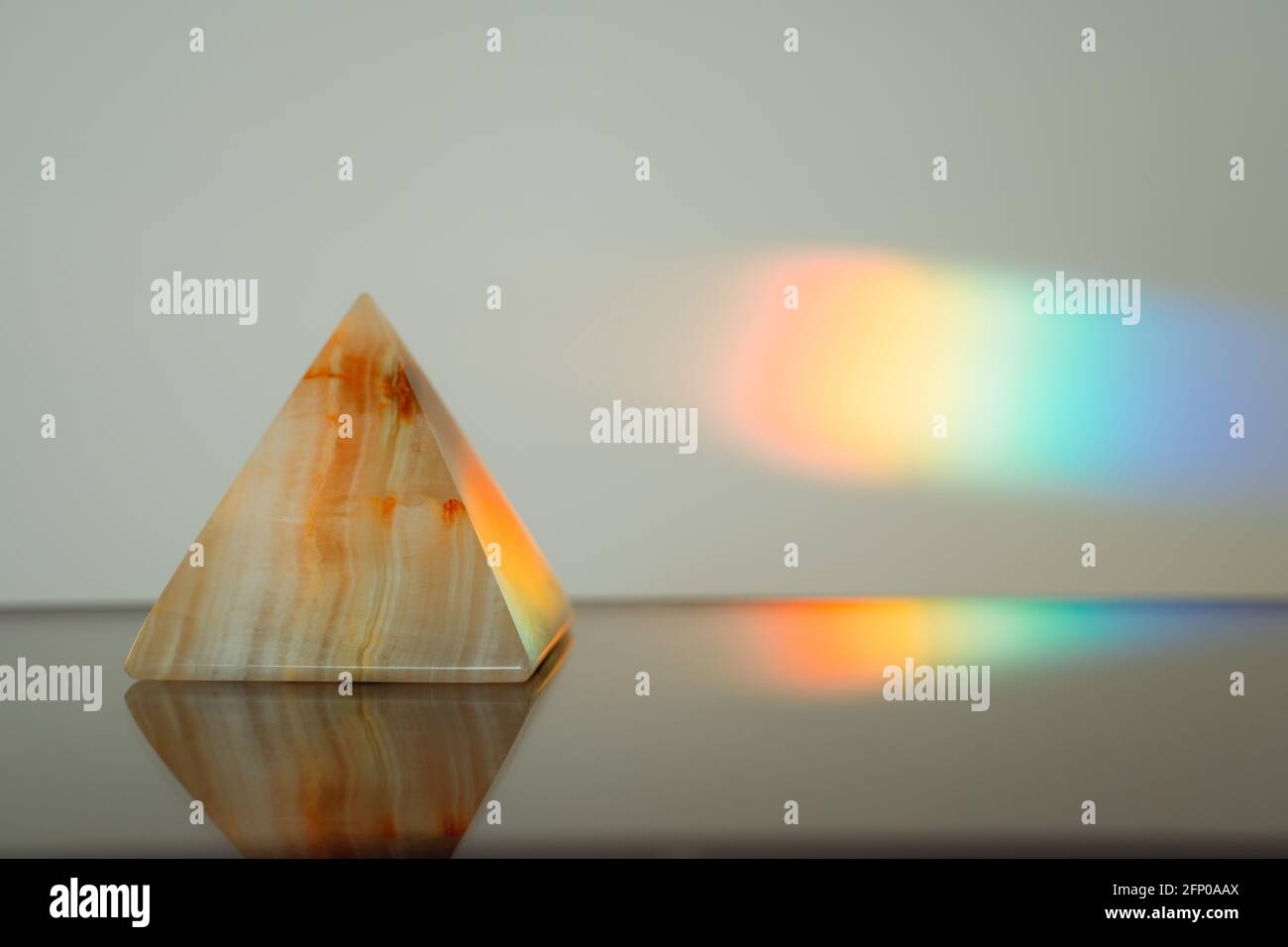 Agate pyramid with a rainbow streak background on a reflective surface Stock Photo