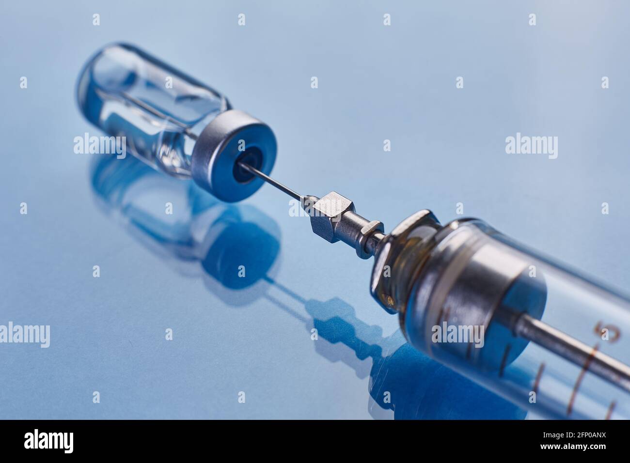 Glass vaccine vial and glass medical syringe on blue glass background ...